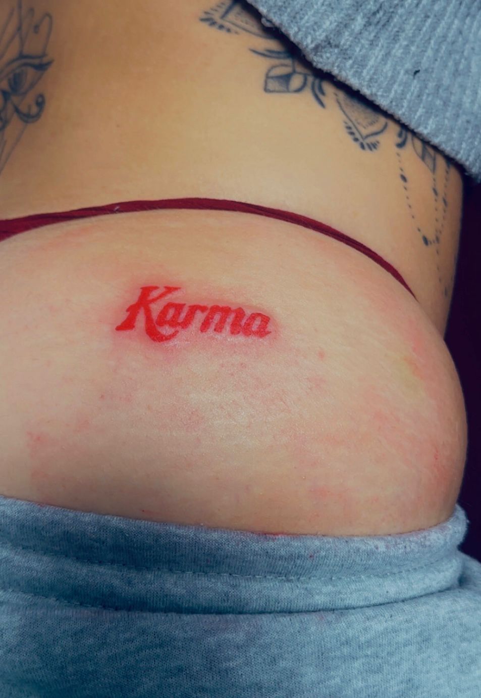 Tatouage encre rouge Karma style retro sur hanche Hakuna Tattoo Arpajon