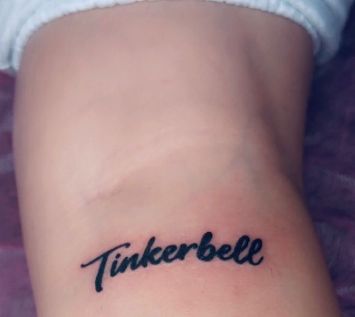Tatouage lettering Tinkerbell en script cursif noir sur le bras Hakuna Tattoo